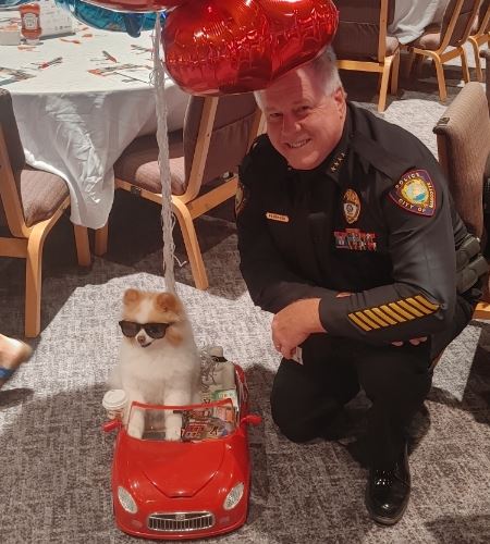 Police officer posing next to tiny dog in a convertible toy car